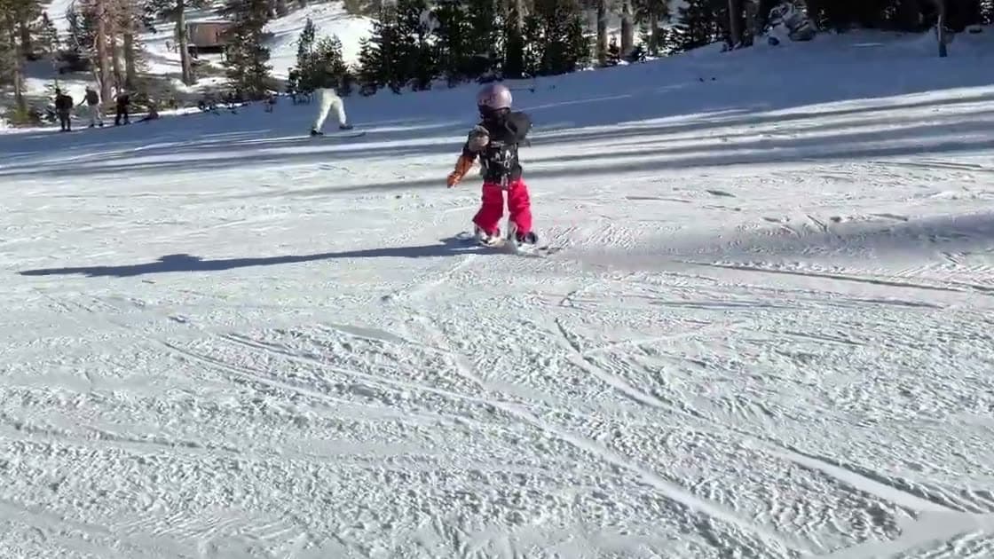 Young child snowboarding on her own down a groomed run, no leash